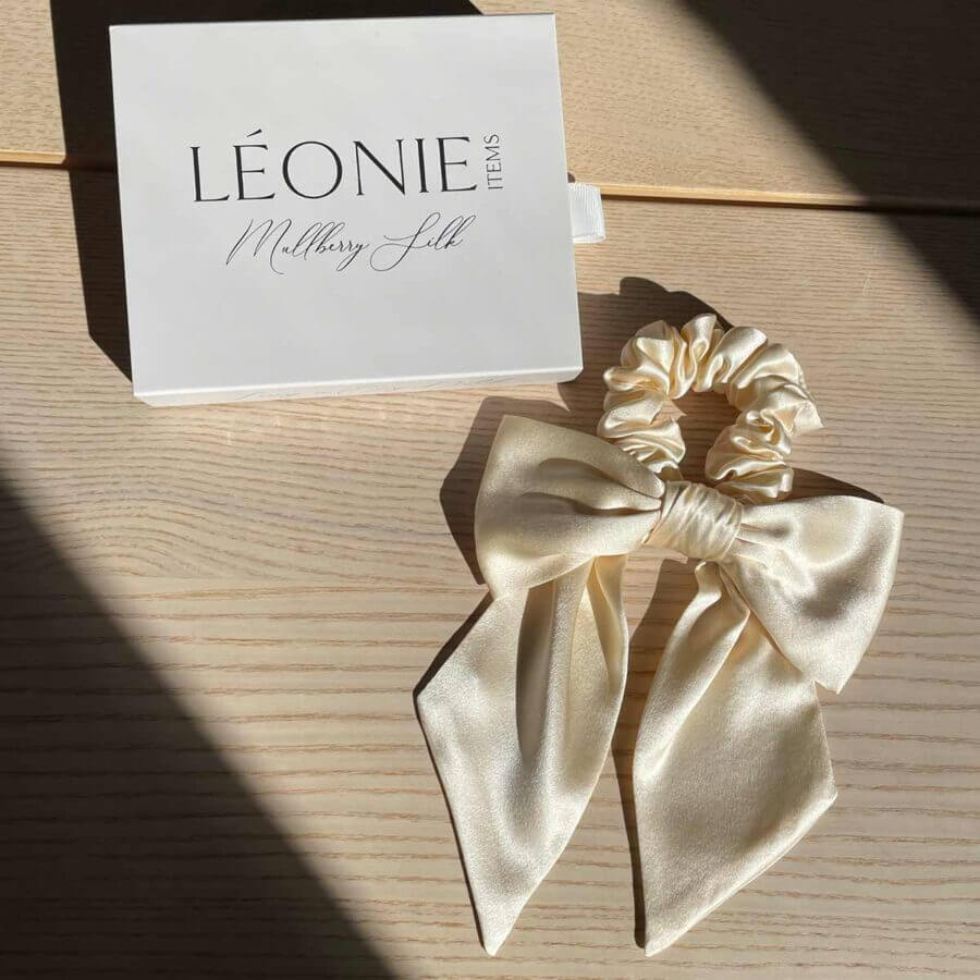 Champagnefärgad sidenrosett-scrunchie i 100 % mullbärssilke – stylad med Léonie Items presentask i solljus