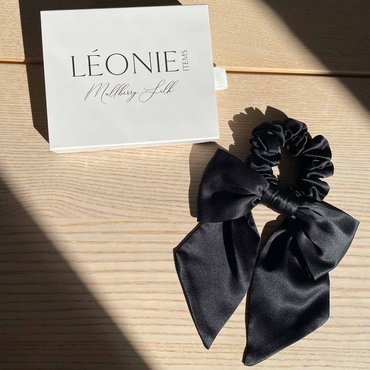 Svart sidenrosett-scrunchie i mullbärssilke – stylad med Léonie Items presentask i solljus